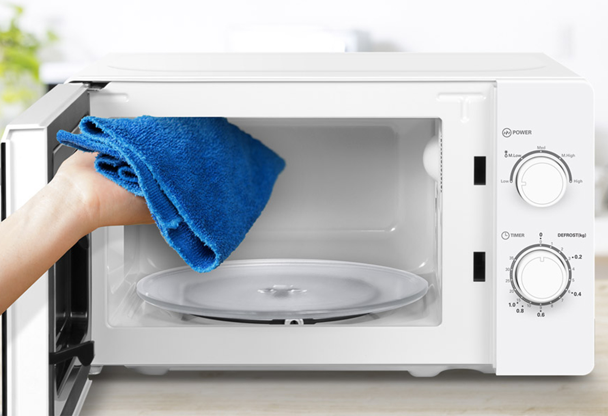 Απεικονίζεται ένα χέρι με μπλε πανί, το οποίο καθαρίζει τον φούρνο μικροκυμμάτων